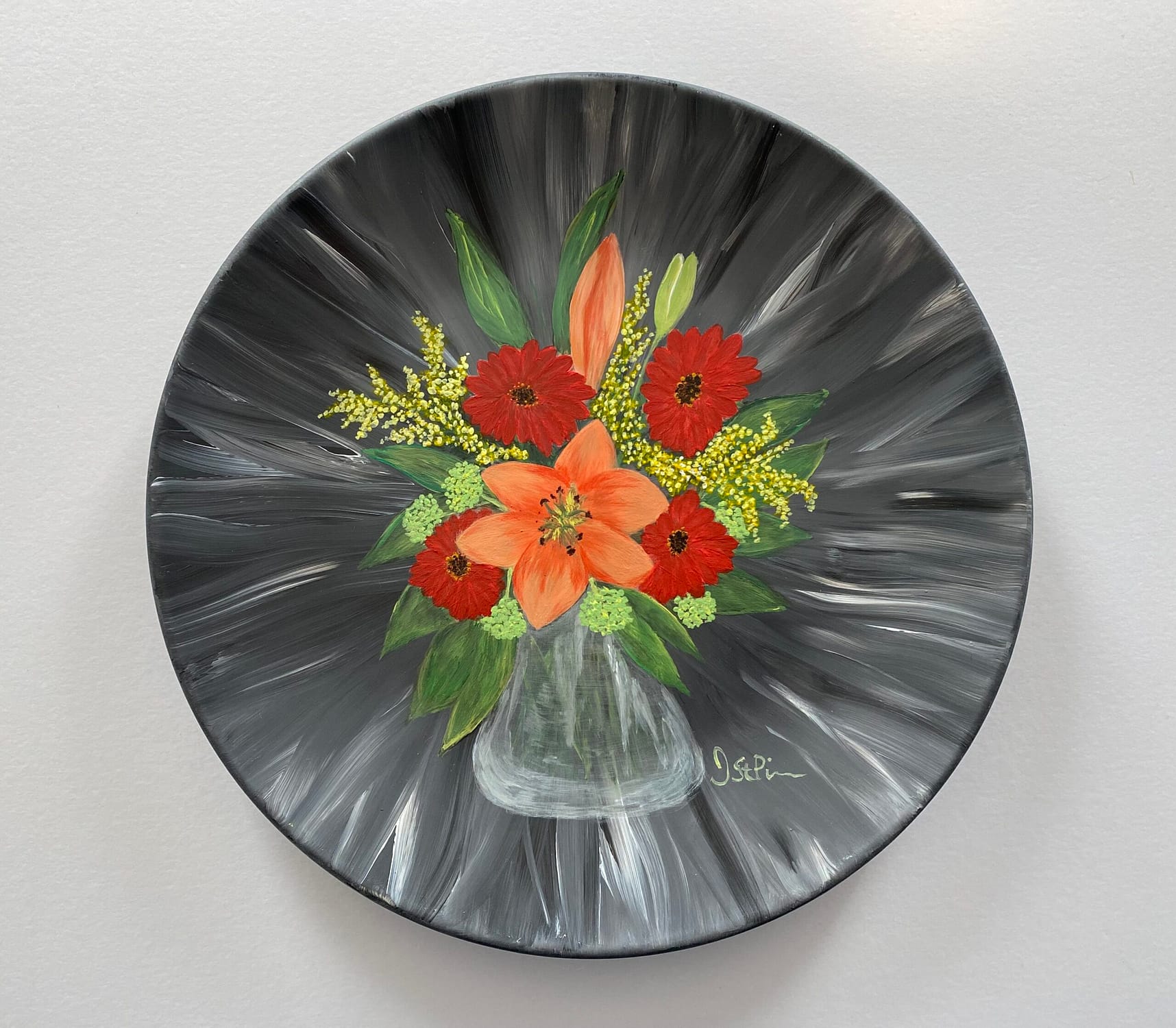 Photo of a black hand painted plate with mixed orange and red flowers in a clear glass vase