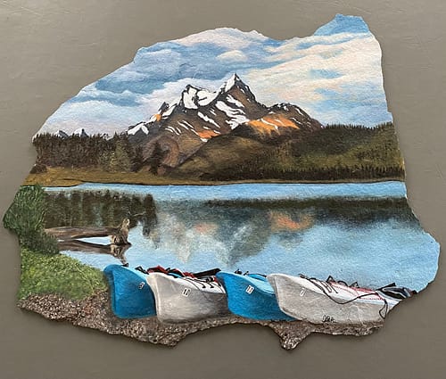 A photo of a large piece of slate stone, hand painted with a mountain and water scene