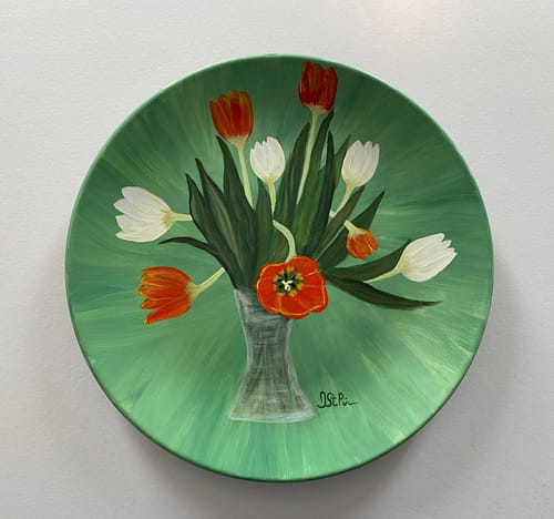 Photo of a green plate hand painted with orange and white twisting tulips in a glass vase