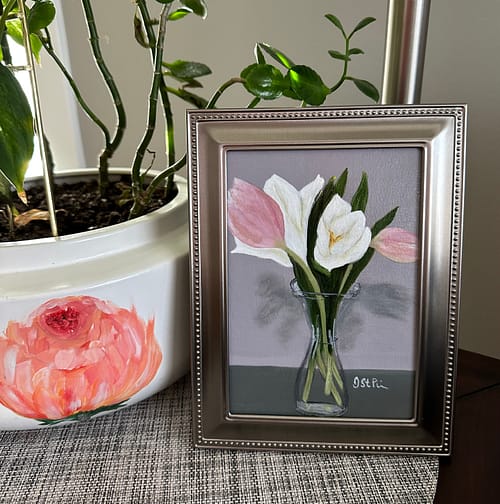 A small framed painting of pink and white tulips in a carafe