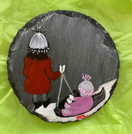 Coaster painted with an image of a girl and her sister sledding.