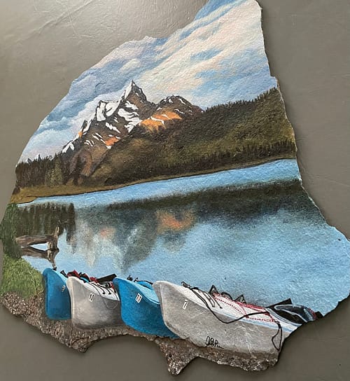 A photo of a large piece of slate stone, hand painted with a mountain and water scene