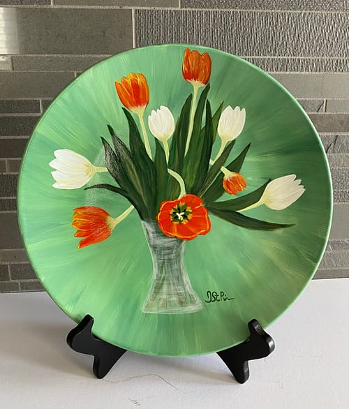 Photo of a green plate hand painted with orange and white twisting tulips in a glass vase