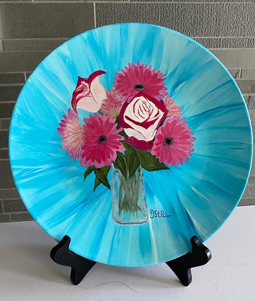 Photo of a Turquoise plate hand painted with Pink Roses and Gerbera Daisies in a glass vase