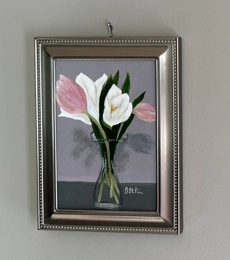 A small framed painting of pink and white tulips in a carafe